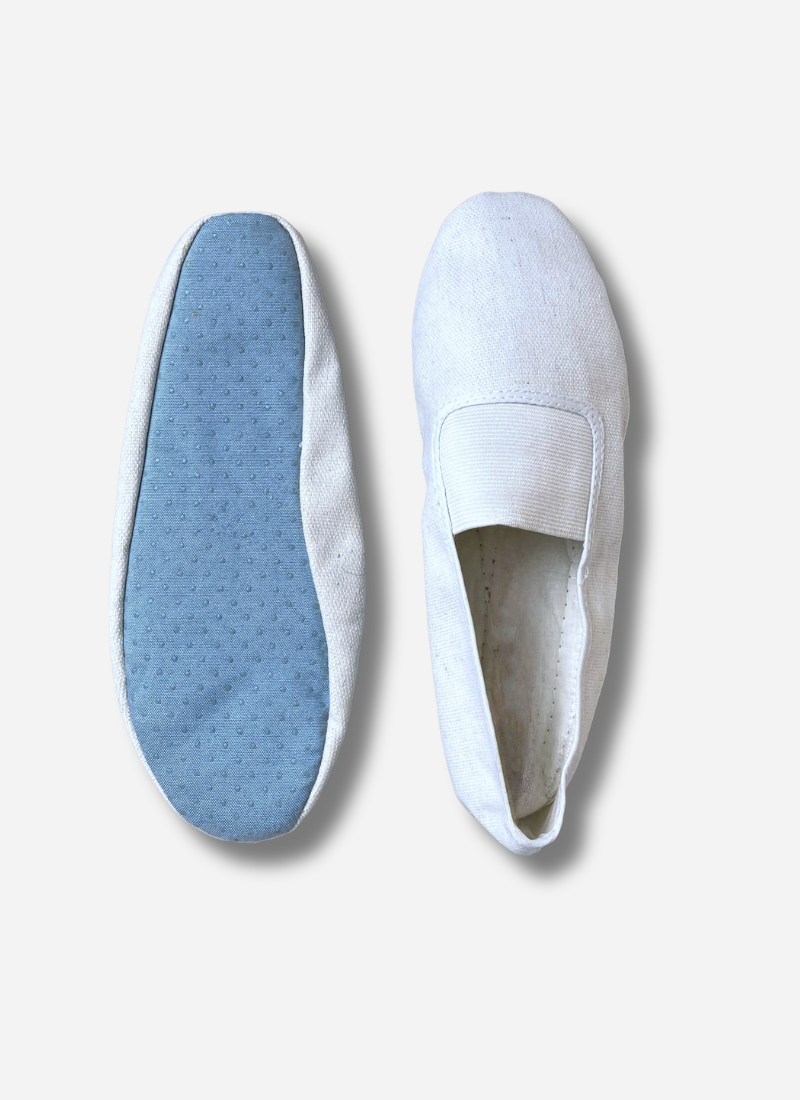Two white adults canvas gymnastics and dance slippers shown side-by-side against a plain background. One shoe shows the top view with the elastic strap; the other shows the light blue, anti-slip textured sole.