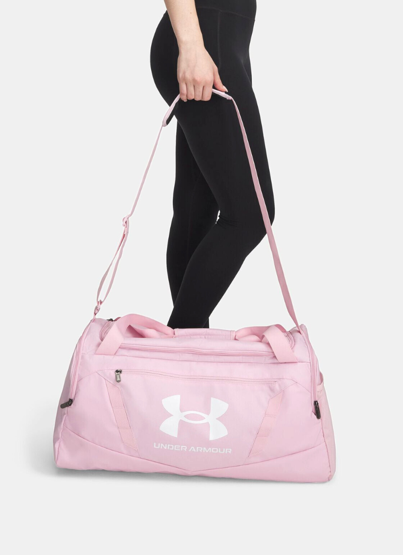 Pink Under Armour duffel bag held by a person on a light gray background