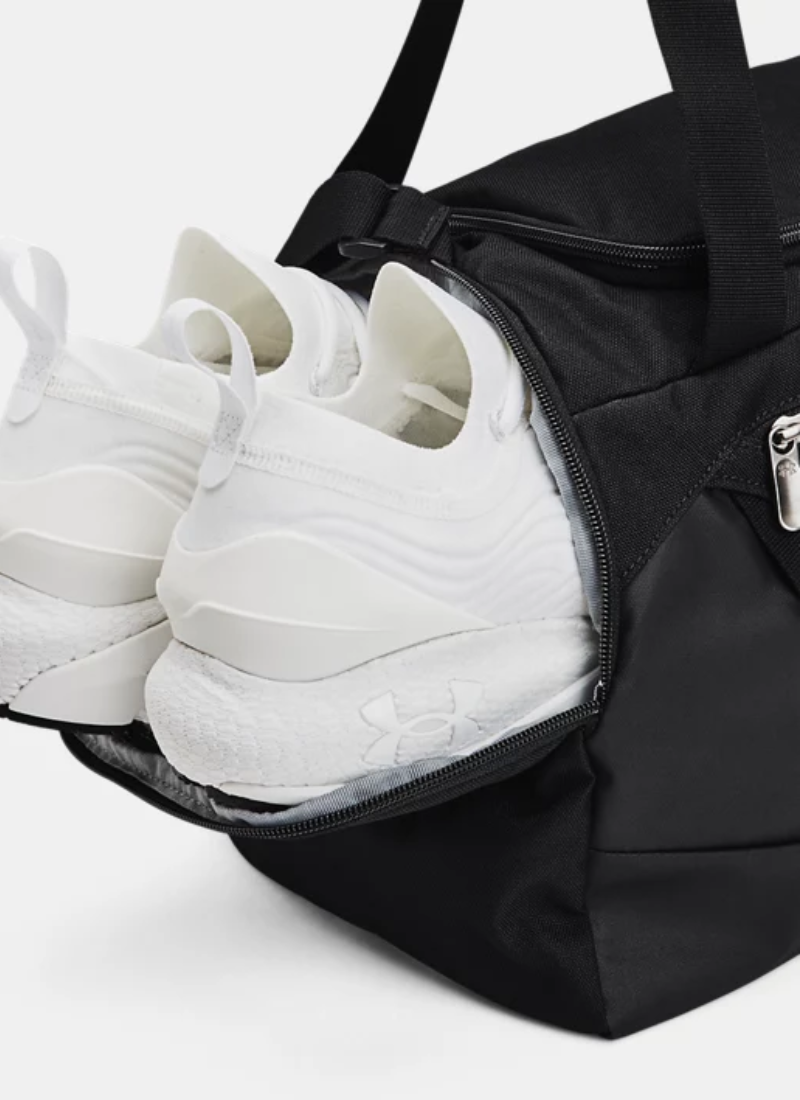 Black duffel bag with white sneakers inside on a light gray background