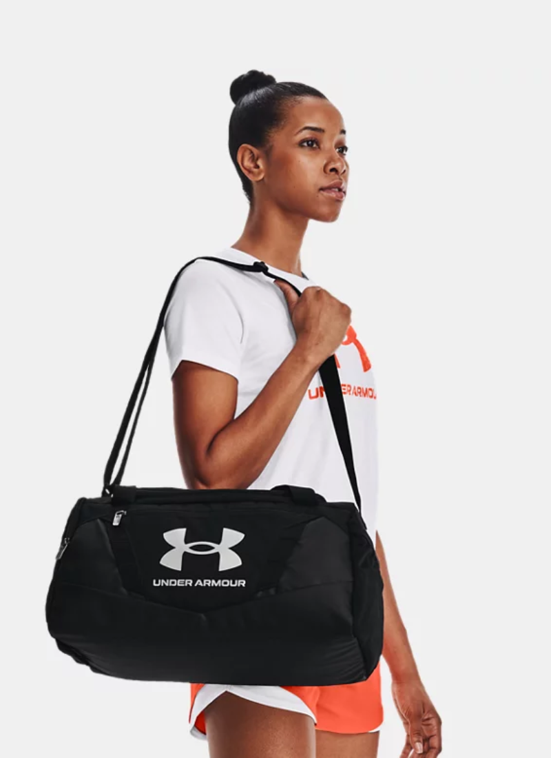 Woman holding a black Under Armour duffle bag against a white background
