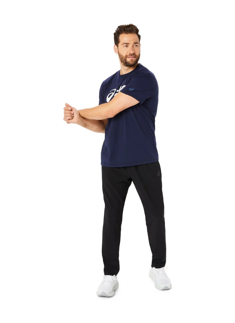 Man wearing a navy blue t-shirt with a logo and black pants on a white background, full shot