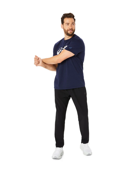 Man wearing a navy blue t-shirt with a logo and black pants on a white background, full shot