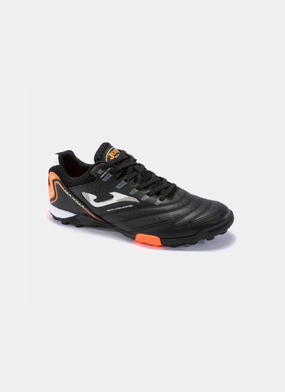 Three-quarter perspective view of the Joma Maxima 2301 turf shoe showing the black synthetic upper, white Joma logo, orange tongue branding, and multi-studded turf rubber sole.