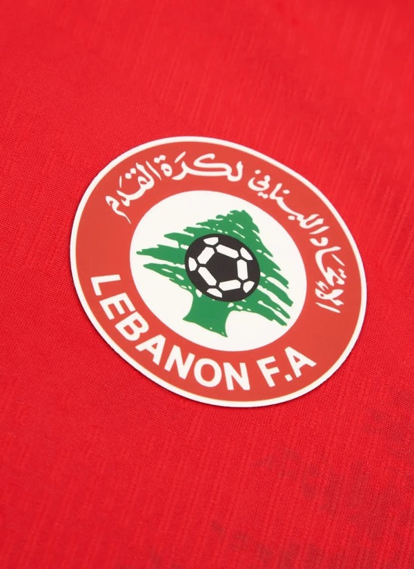 Close-up view of the circular Lebanon Football Association crest featuring a green cedar tree and football on a red textured kit.