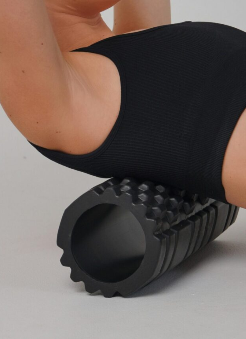 Woman using black textured foam roller on lower back