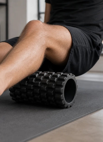 Man rolling calf on black textured foam roller on yoga mat