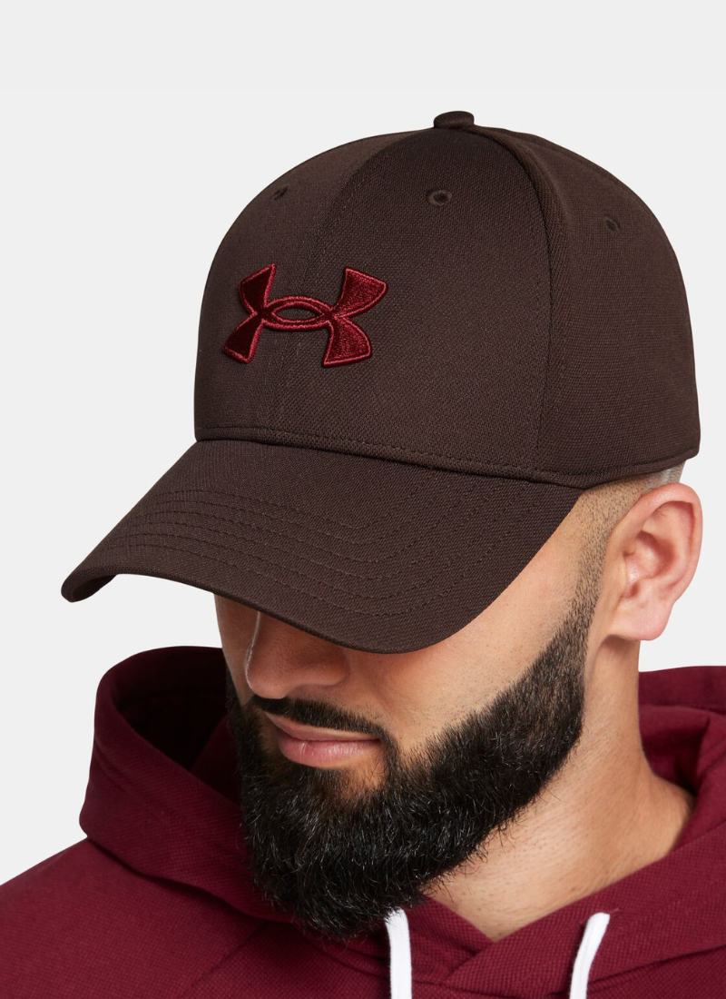 Man wearing a brown cap with a red Under Armour logo and matching hoodie on a light gray background
