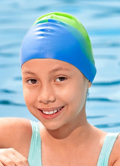 A smiling young girl wearing a blue and green gradient swim cap, with water ripples in the background.