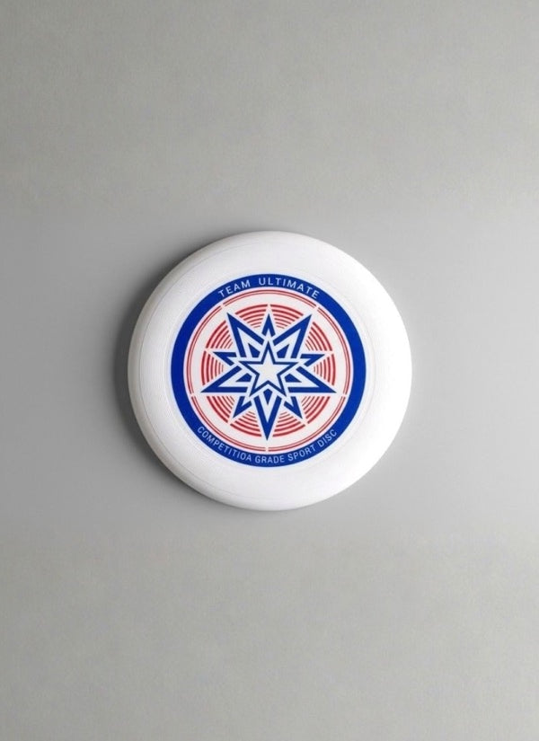 White flying disc with a blue and red star graphic and "Team Ultimate" print on a plain grey background