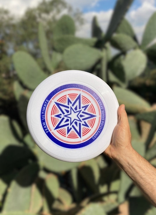 Hand holding a white flying disc with a blue and red star graphic in front of prickly pear cactus