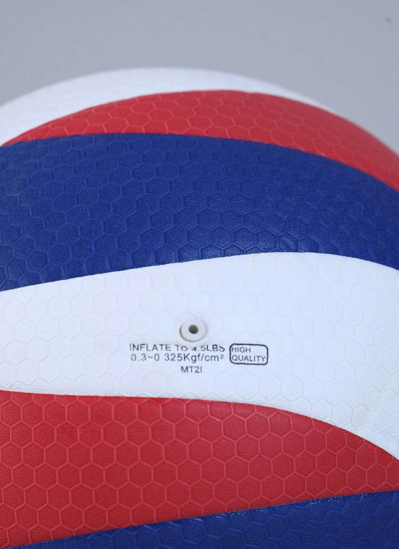 A close-up of the inflation valve on the red, white, and blue Gold Cup volleyball, showing a hexagonal surface texture and printed inflation pressure guidelines.